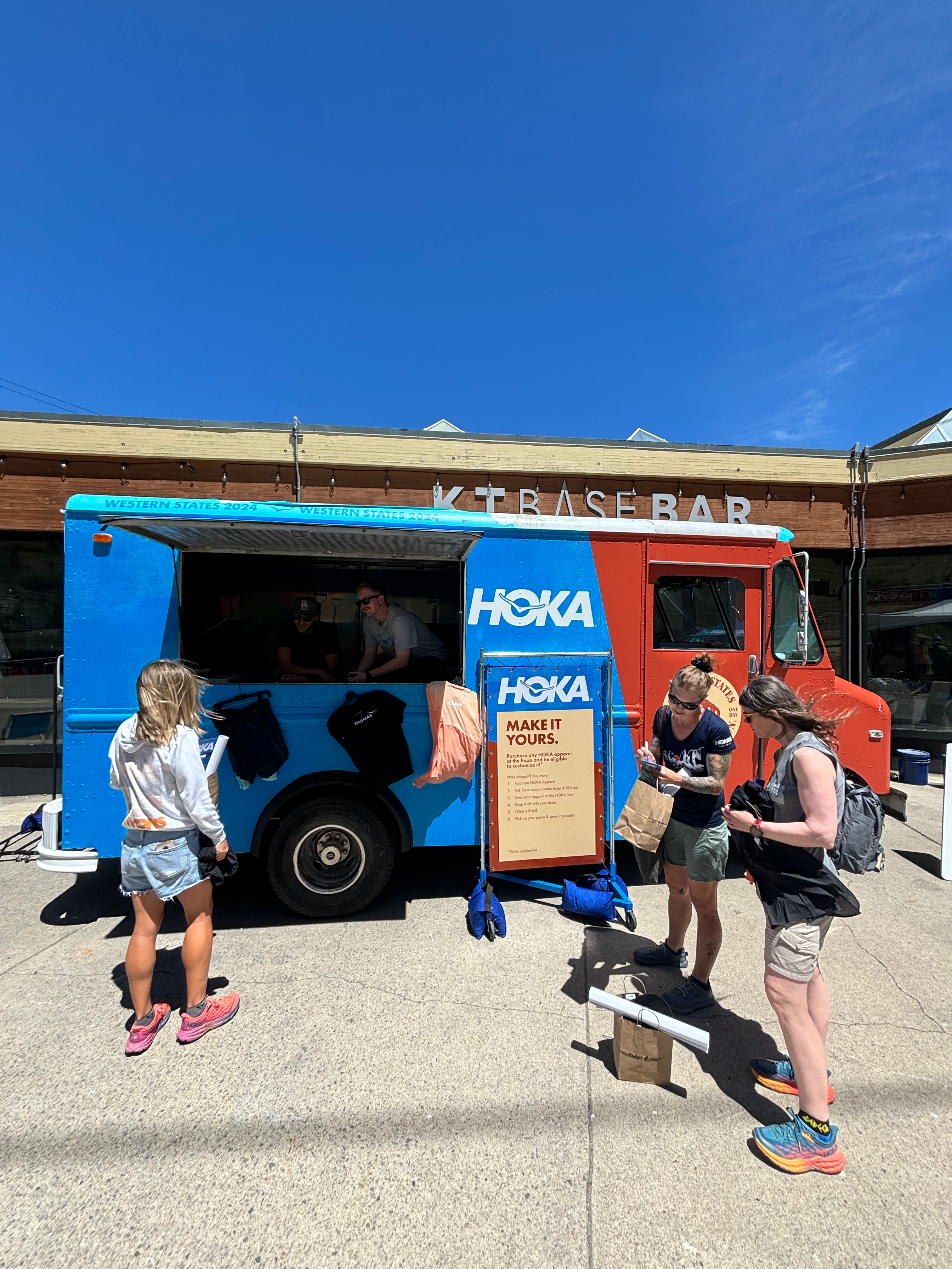 People interacting with a Hoka branded like food truck that live screen prints on promotional products on a sunny day in Truckee Ca.